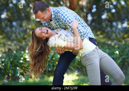 Er zieht mich von den Füßen. Ein liebevolles Paar draußen in der Sommersonne. Stockfoto