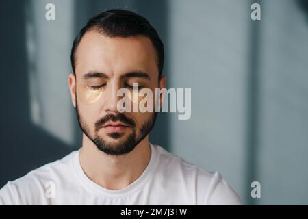 Entspannter, gutaussehender Mann, der mit geschlossenen Augen sitzt und meditiert, während er allein zu Hause ist. Ruhe und Entspannung Freizeit, keine Angst und Stress Stockfoto