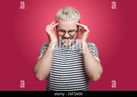 Vorderansicht eines Mannes mit Brille, der müde ist und Kopfschmerzen hat, isoliert auf pinkfarbenem Hintergrund. Stockfoto
