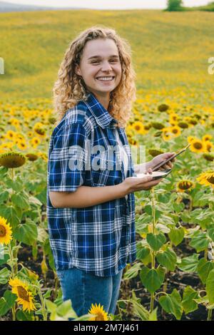 Landwirtin mit Tablet auf dem Sonnenblumenfeld. Konzept einer modernen intelligenten Landwirtschaft durch den Einsatz von Elektronik, Technologie und mobilen Apps in der Landwirtschaft Stockfoto