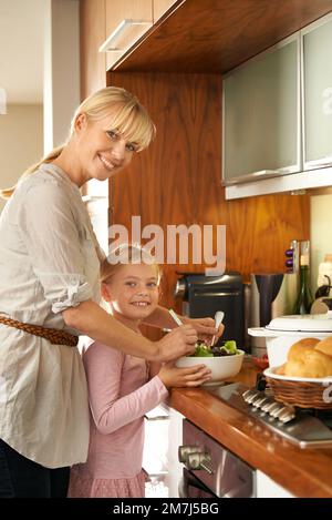 Mommys kleine Helferin. Ein süßes Mädchen und ihre Mutter kochen in der Küche. Stockfoto