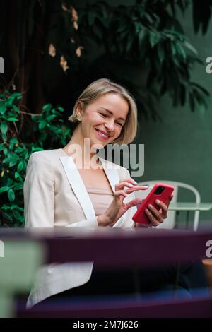 Lächelnde Frau, während sie ein Mobiltelefon benutzte und draußen in einem Café saß. Stockfoto