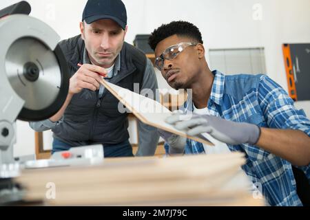 Vorarbeiter, der mit der Kreissäge die Holzkante des Lehrlings prüft Stockfoto