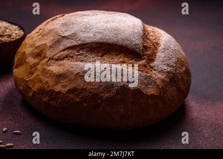 Wunderschönes, köstliches, frisch gebackenes, rundes Weißbrot auf dunklem Betonhintergrund Stockfoto