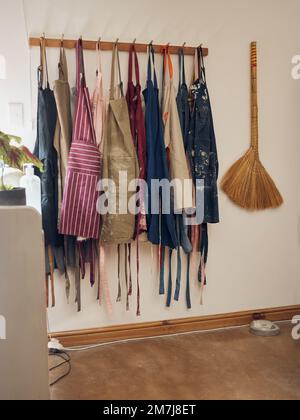 Kleiderständer, Schürze und Töpferwaren mit Besen in einer leeren Werkstatt oder einem Studio gegen Still Life Wand für Design. Kreativität, Kunst und Kleidung mit einem Stockfoto
