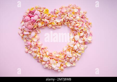 Herz aus rosa-gelben Rosenblättern. Rosenblütenblätter Herz auf pinkfarbenem Hintergrund. Draufsicht mit Kopierbereich für Ihren Text. Liebe und romantisches Konzept. Stockfoto