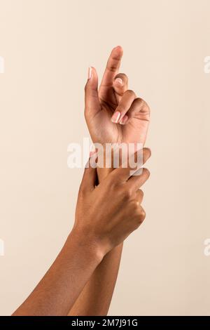 Hände einer afroamerikanischen Frau, die sich das Handgelenk berührt und eine perfekte Maniküre vor beigefarbenem Hintergrund zeigt Stockfoto