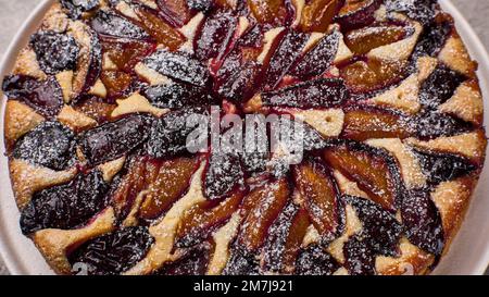 Panoramablick auf hausgemachte Torte oder Kuchen mit Pflaumen auf weißem Teller Stockfoto