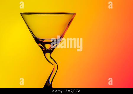 Wunderschönes konisches Cocktailglas mit einem ungewöhnlichen, gebogenen Stiel, fotografiert auf einem farbigen Hintergrund, das ein Beugungsmuster erzeugt Stockfoto