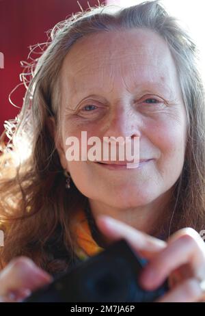 Eine freundliche 63-jährige Frau ohne Make-up mit einer Kamera in der Hand schaut in die Kamera Stockfoto