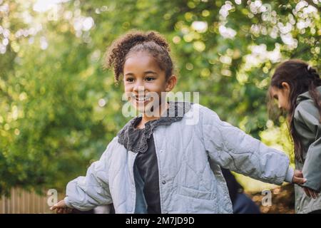 Glückliches Mädchen, das im Park mit ausgestreckten Armen wegsieht Stockfoto