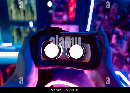 Blickwinkel auf die Hände einer Person, die ein 3D 360-Virtual-Reality-Headset trägt, Augmented-Reality-Brille in einer futuristischen Umgebung mit Neonlicht. VR AR – Hintergrund zur Innovationstechnologie Stockfoto