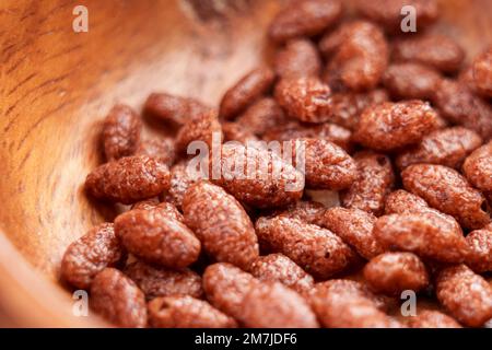 Schokoladenflocken aus gepufftem Reis in rustikaler Holzschüssel. Knuspriges Schokoladenfrühstück. Makro Stockfoto