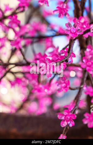 Weihnachtsbeleuchtung in Form einer rosafarbenen Blume auf einem Ast einer Stadtstraße Stockfoto
