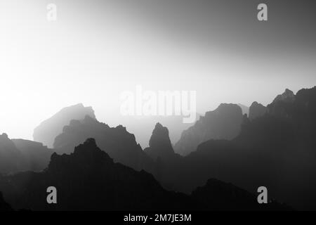 Ein Luftblick auf felsige Berge bei einem nebligen Tag, der in Graustufen aufgenommen wurde Stockfoto