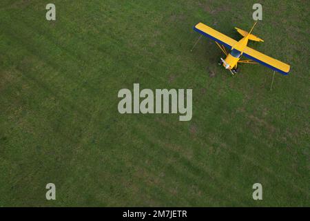 Kleines gelbes Flugzeug, das für Kurzstreckenflüge von oben gesehen wird und auf einem grünen Feld geparkt ist Stockfoto