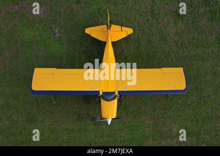 Kleines gelbes Flugzeug, das für Kurzstreckenflüge von oben gesehen wird und auf einem grünen Feld geparkt ist Stockfoto