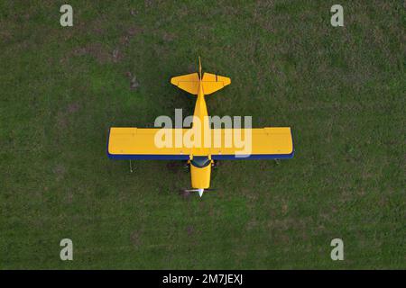 Kleines gelbes Flugzeug, das für Kurzstreckenflüge von oben gesehen wird und auf einem grünen Feld geparkt ist Stockfoto