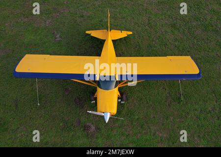 Kleines gelbes Flugzeug, das für Kurzstreckenflüge von oben gesehen wird und auf einem grünen Feld geparkt ist Stockfoto