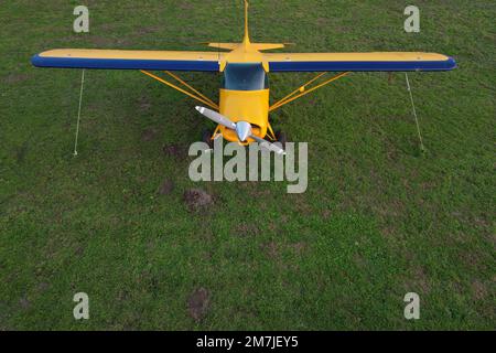 Kleines gelbes Flugzeug, das für Kurzstreckenflüge von oben gesehen wird und auf einem grünen Feld geparkt ist Stockfoto