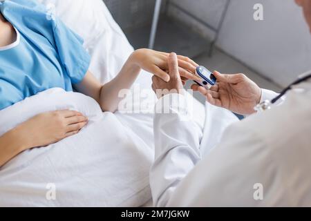 Schnittbild eines leitenden Arztes, der ein Pulsoxymeter an der Hand des Patienten in der Klinik trägt, Stockbild Stockfoto