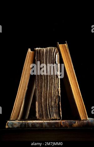 Vertikale Nahaufnahme von drei alten Büchern auf schwarzem Hintergrund