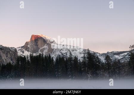 Das letzte Licht der untergehenden Sonne beleuchtet eine schneebedeckte Halbkuppel an einem Winternachmittag. Yosemite Nationalpark. Stockfoto