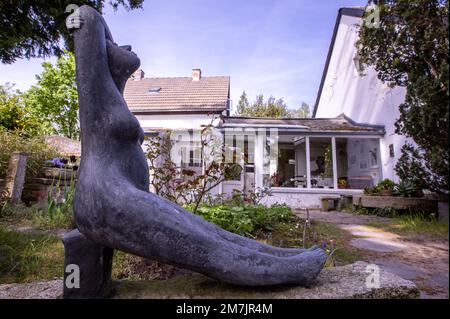 20. Mai 2022, Mecklenburg-Vorpommern, Koserow: Eine Skulptur steht vor dem ehemaligen Studio und Wohnsitz von Otto Niemeyer-Holstein auf dem Künstlergut in Lüttenort auf der Ostseeinsel Usedom. Der Maler hatte einen alten Eisenbahnwaggon als Sommerdomizil eingerichtet und dann seine Wohnräume und sein Studio gebaut. In diesem Sommer zeigt das Museum Werke aus der Malersammlung unter dem Titel „Usedom - in the Mirror of Mainting and Graphics“. Der 1896 in Kiel geborene Maler Otto Niemeyer ließ sich 1933 auf Usedom nieder und fand dort seine Motive. Sein Anwesen ist jetzt ein Museum. Fotopapier Stockfoto