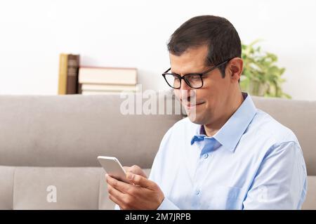 Foto eines glücklichen Mannes mittleren Alters, der zu Hause ein Smartphone benutzt Stockfoto