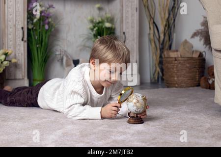 Süßes kleines, kleines, blondes Kind, Junge, erforscht die Welt mit Lupe, lernt Kontinente Stockfoto