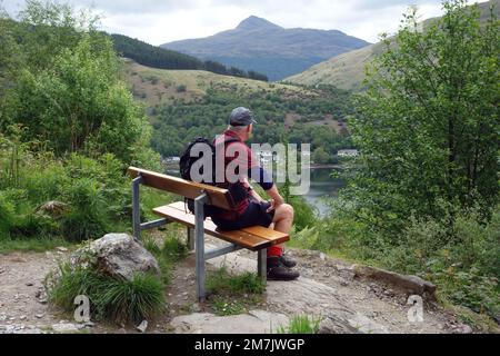 Old man Sat auf der Bench über Loch Long in der Nähe von Arrochar mit Blick auf den Scottish Mountain Munro „Ben Lomond“ in den schottischen Highlands, Schottland. Stockfoto