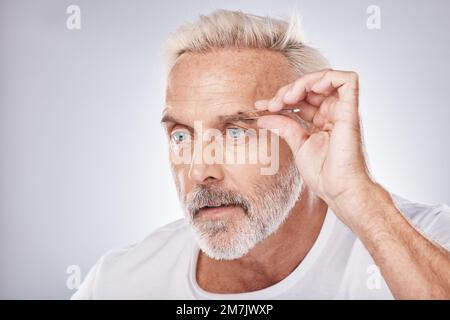 Männergesicht, Hand oder pinzende Augenbraue bei der Pflege auf grauem Studiohintergrund, Gesichtspflege oder Wellness-Beauty-Ästhetik. Kopfschuss, ausgereiftes Modell oder Stockfoto