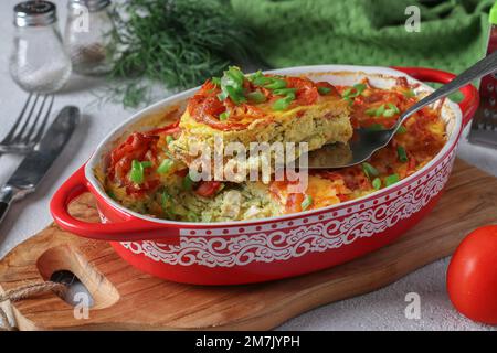 Hausgemachter Zucchini-Auflauf mit Huhn, Tomaten und Käse in einer Keramikform auf Holzbrett Stockfoto