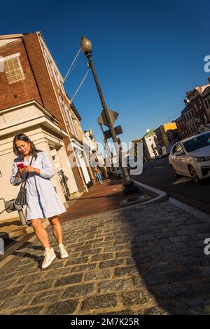 Eine Frau, die auf ihr Telefon schaut, ist die angesagte, gehobene Wisconsin Avenue mit schicken Geschäften und Restaurants in Georgetown, einem historischen Viertel, und Kommerzen Stockfoto