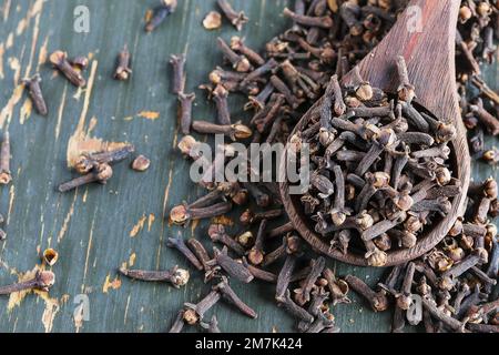 Getrocknete Nelken in einem Holzlöffel und auf einem rustikalen Holztisch verstreut. Draufsicht auf Gewürze. Stockfoto