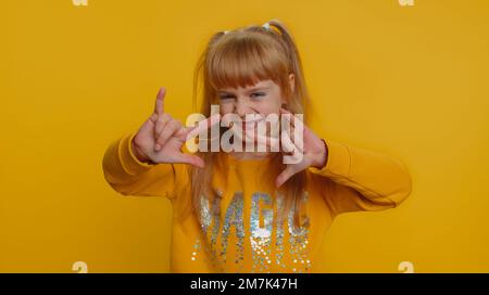 Ein überfreuliches, glückliches Mädchen, das Rock 'n' Roll-Geste mit Händen zeigt, ein cooles Schild, schreit ja mit verrücktem Ausdruck, tanzt, freut sich über den Erfolg. Kleine Kleinkinder auf gelbem Hintergrund Stockfoto