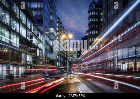 Abendlicher Blick auf eine geschäftige Straße in der City of London mit Ampelpfaden Stockfoto