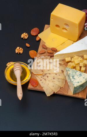 Verschiedene Käsesorten auf einem Holzbrett mit Honig, Trauben, getrockneten Aprikosen und Nüssen Stockfoto