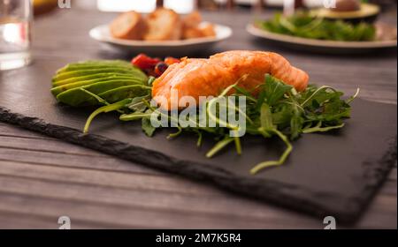 Gebackenes Meerforellenfilet mit frischem Gemüse und Kräutern auf schwarzem Brett Stockfoto