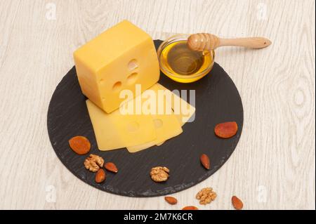emmentaler Käse und auf schwarzem Graphitbrett mit Honig und Nüssen geschnitten Stockfoto