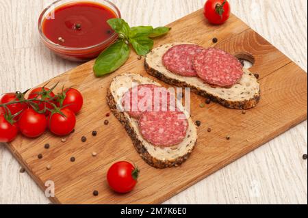 Sandwiches mit Räucherwurst und Käse auf einem Holzbrett, dekoriert mit Kirschtomaten und Basilikum Stockfoto