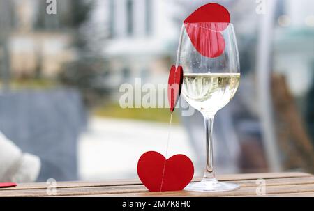 Papier rote Herzen Girlande in Frauenhänden Holzbretttisch, hellblaues Metall oder Champagnerglas Stockfoto