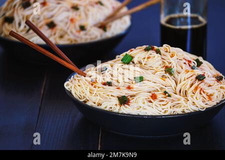 Selektiver Fokus von zwei Schüsseln vegetarischer asiatischer chinesischer Nudeln auf einem schwarzen rustikalen Holztisch mit verschwommenem Vorder- und Hintergrund. Stockfoto