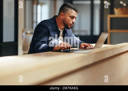 Webdesign-Experte, die in einem Büro mit mehreren Mitarbeitern an einem Laptop arbeitet. Kreativer Geschäftsmann, der auf einem Grafiktablett zeichnet. Männlicher Designer, der Remote-Arbeit macht Stockfoto