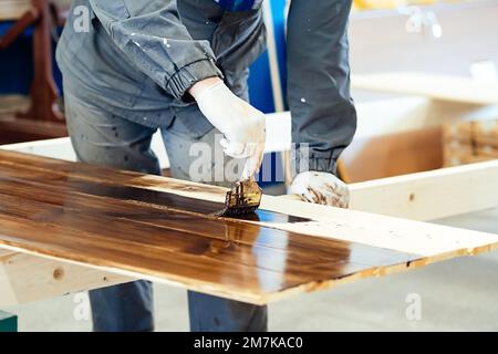 Man malt Holzbretter mit einem Pinsel. Zimmermannsschränke lackieren Holzflächen. Authentischer Workflow... Stockfoto