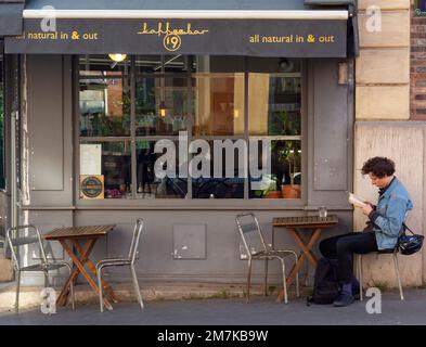 Ein Mann liest sein Buch, während er auf der Außenterrasse des Pariser Cafés sitzt Stockfoto