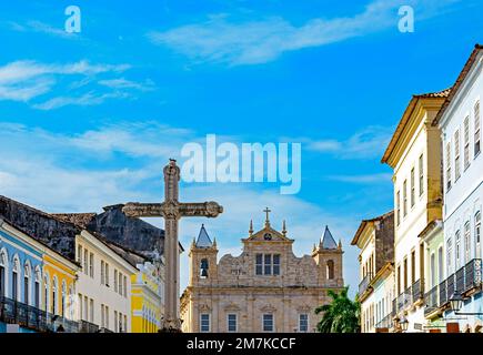 Großes Kruzifix auf dem zentralen Platz des historischen Viertels Pelourinho in der Stadt Salvador in Bahia mit Barockkirche und Kolonialhäusern i. Stockfoto