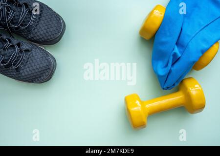 Leichte, moderne Sportschuhe aus Textil mit trendigen gelben Kurzhanteln und einem kleinen Handtuch. Flacher Kopierbereich. Gewichtskontrolle und gesunder Lebensstil. Stockfoto