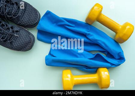 Leichte, moderne Sportschuhe aus Textil mit trendigen gelben Kurzhanteln und einem kleinen Handtuch. Flacher Kopierbereich. Gewichtskontrolle und gesunder Lebensstil. Stockfoto