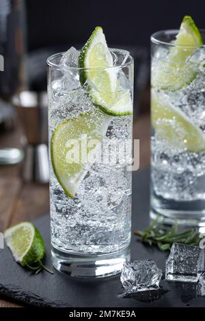 Gin-Tonic-Cocktail mit Limettenscheiben und Eis in einem hohen Glas auf einem schwarzen Schieferbrett Stockfoto